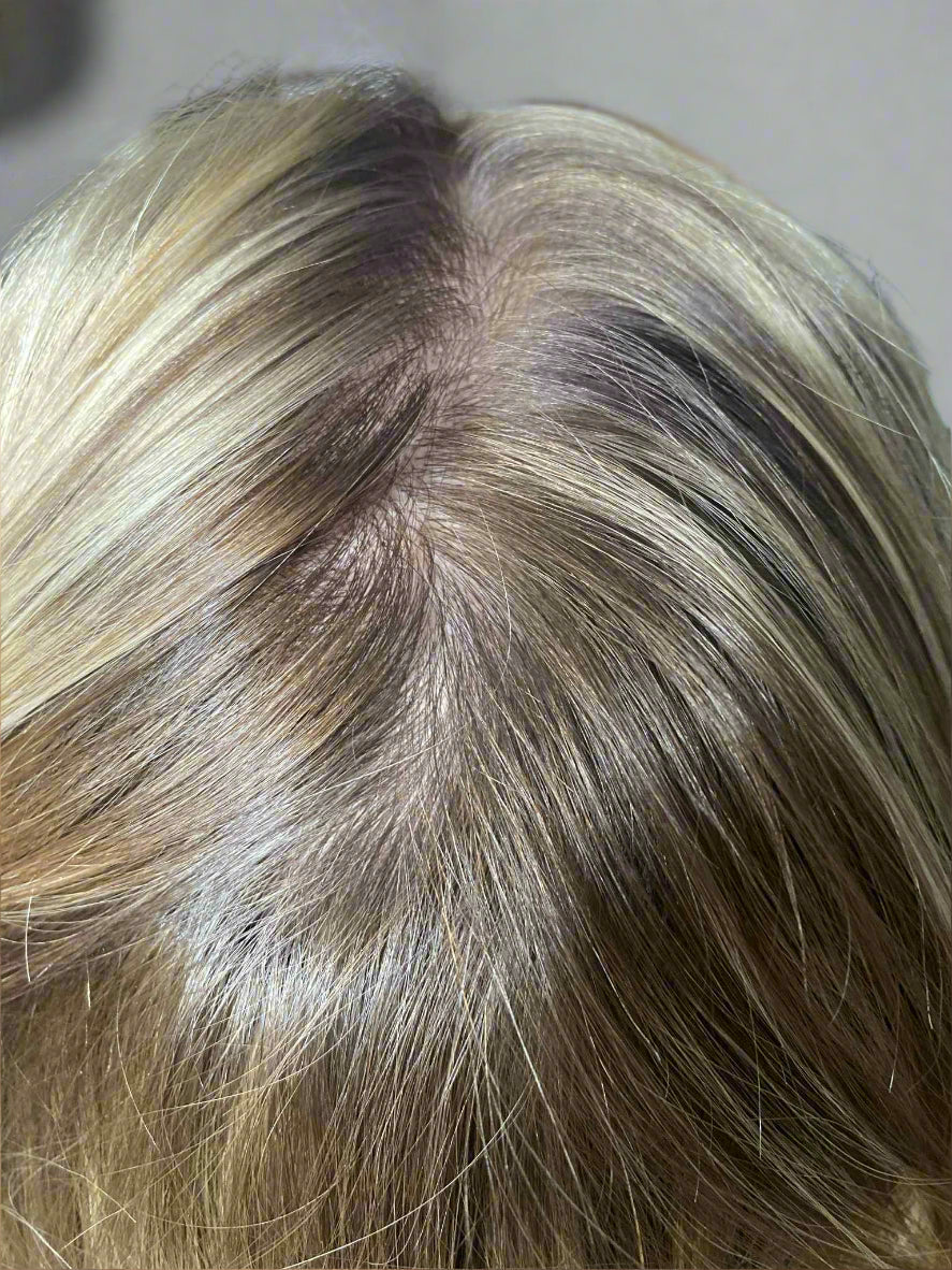 Close-up of a person's head with blonde hair and a visible part line.